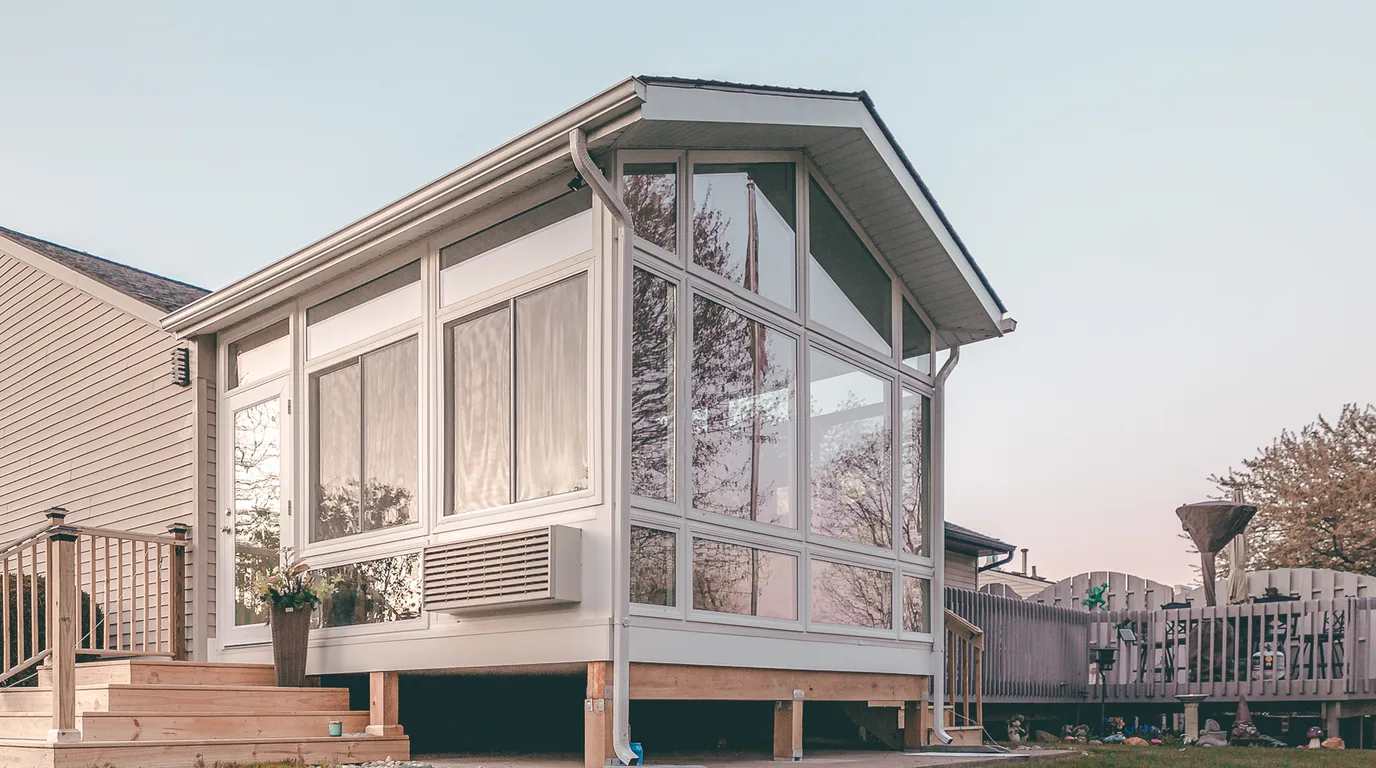 A finished four-season sunroom addition on a real home, daylight on the glass and a deck running off the far end.