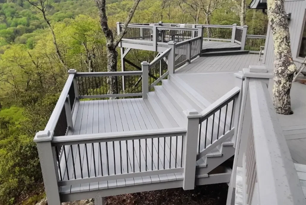 A finished composite deck with railings and stairs stepping down into a wooded lot