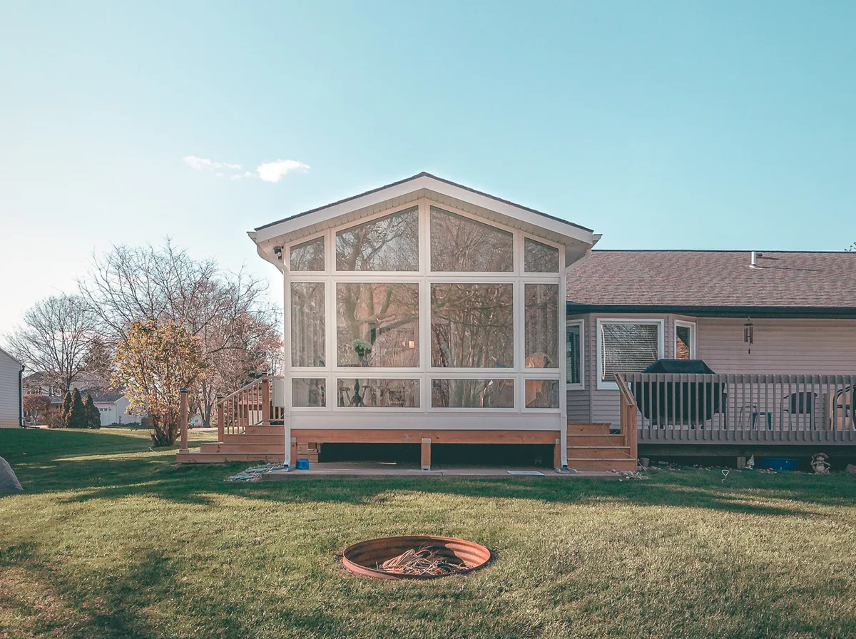 A gable-roofed sunroom addition on a real home, seen across the lawn from a backyard fire ring