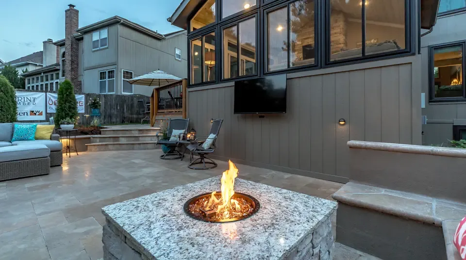 A finished patio at dusk with a lit fire table and a glowing house behind it, the kind of work Atlantic Media markets