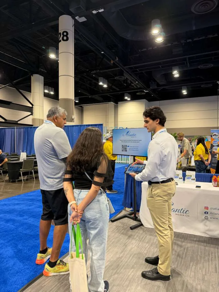 An Atlantic Media Company team member showing a tablet to a couple at the trade-show booth