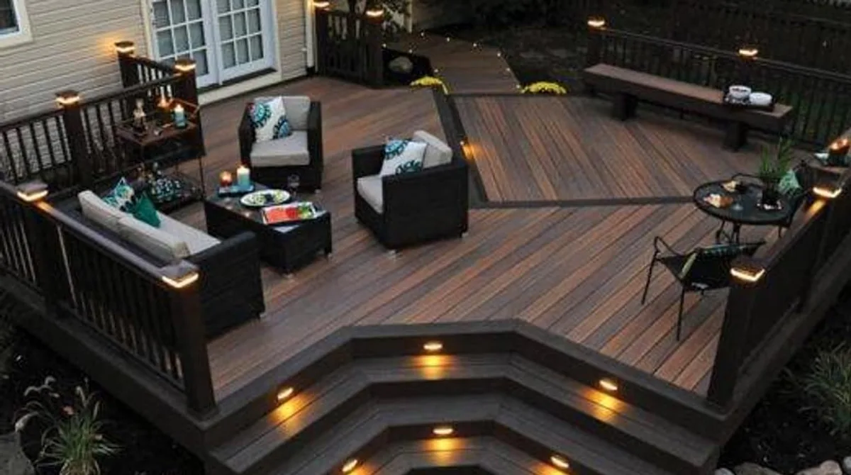 A premium composite deck at dusk with integrated riser lighting, clean board pattern, railings, level changes, and simple outdoor furniture.