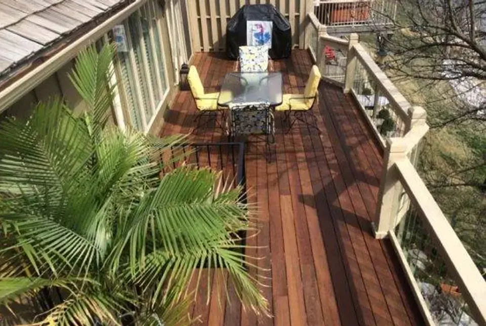 A finished hardwood deck seen from above, showing board run, railing detail, and a dining set in place.