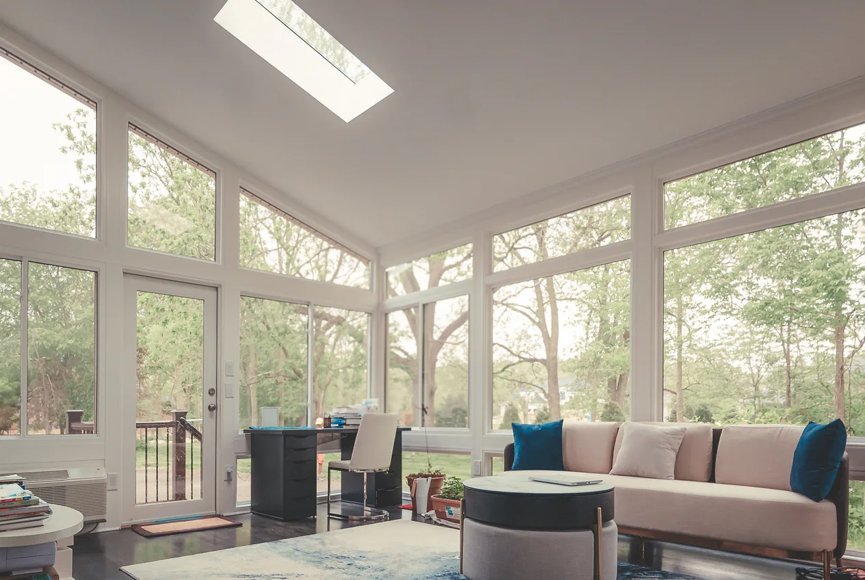 The interior of a finished four-season sunroom, glass on three sides and a vaulted ceiling with daylight crossing the floor.