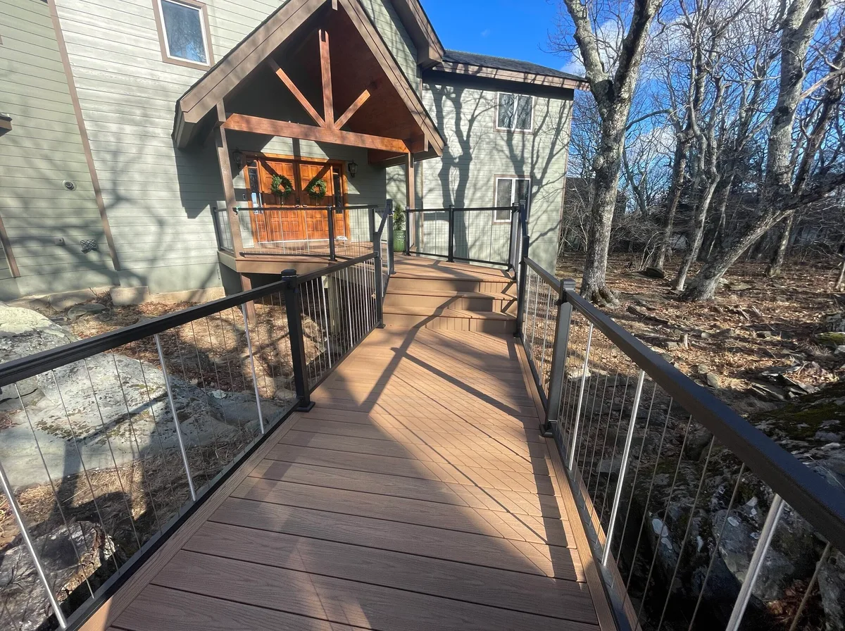 A cable-railed deck walkway running along a house into a wooded lot