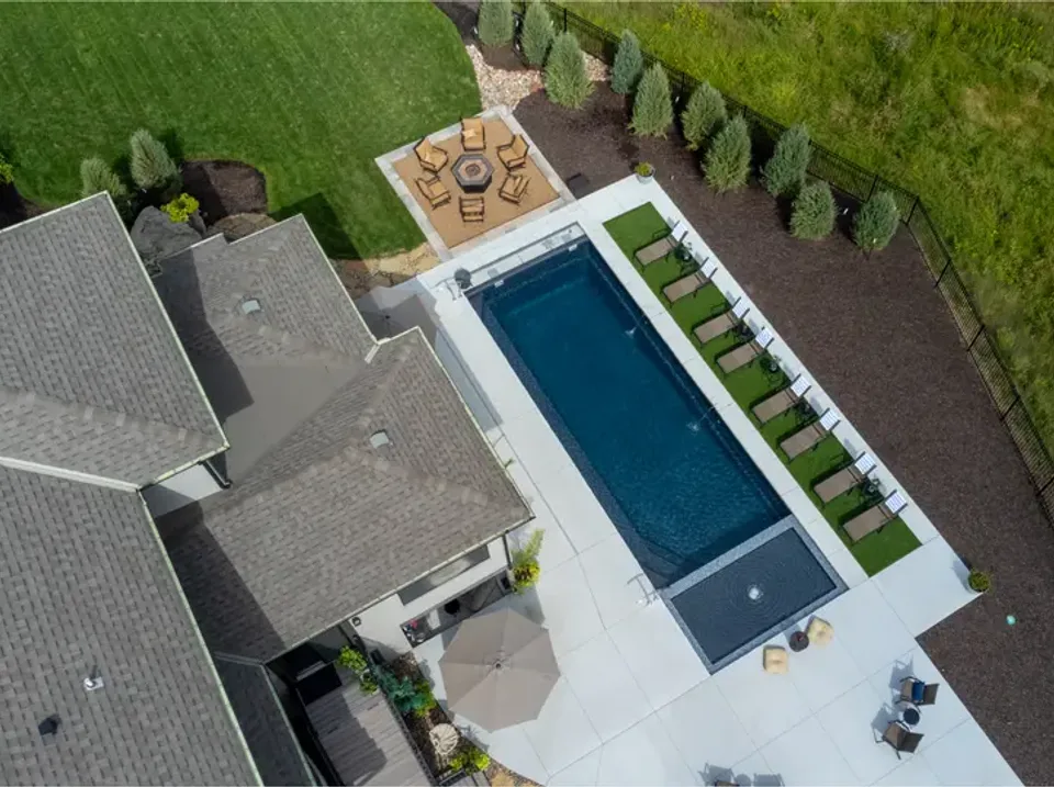 An aerial view of a rectangular inground pool set into a paved patio beside the house