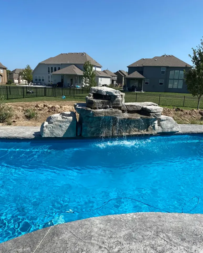 A freeform pool with a natural rock waterfall feature, photographed in bright daylight